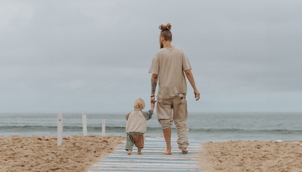 Wojtek, który dumnie kroczy za rękę z Zoją po plaży w kierunku morza w San Sebastian, Hiszpania.