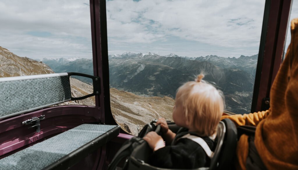 Zoja siedzi w plecaku Thule Sapling z zaciekawieniem obserwujące majestatyczne góry podczas wjazdu kolejką linową na Bettmerhorn.